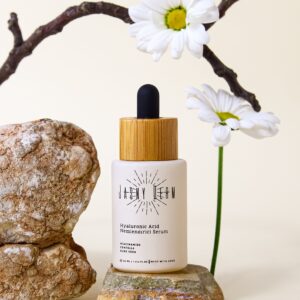 Elegant hyaluronic acid serum bottle surrounded by natural stones and flowers, symbolizing purity and freshness.